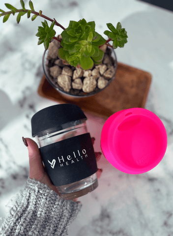 Image of the black hello health glass coffee cup being held over a marble counter top 