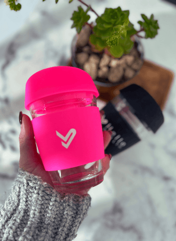 Image of a hot pink glass coffee cup being held with the black version in the background